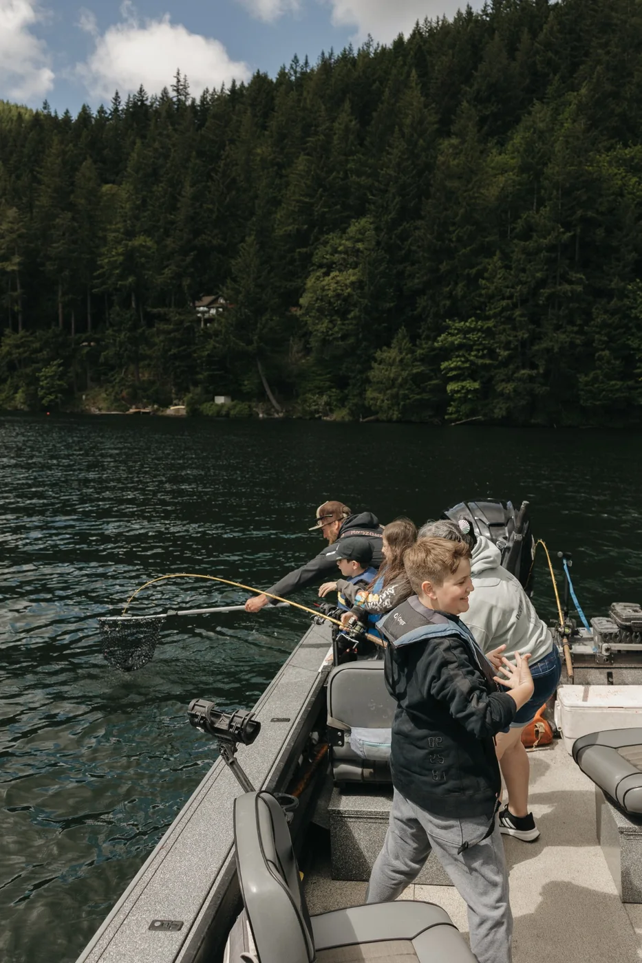 Youth actively fishing from a boat while an instructor helps land a fish