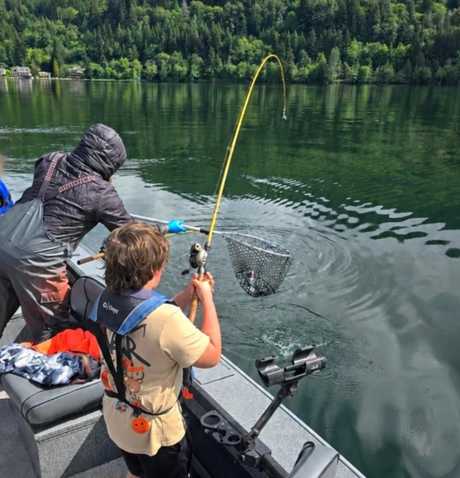 Outdoor instructor helping youth learn to fish from a boat on a Pacific Northwest lake